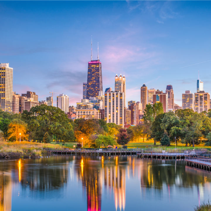 A vibrant view of the Chicago skyline at dusk, with city lights reflecting on a calm waterfront and lush greenery in the foreground—capturing the broader region served by temp staffing and consulting in nearby Rosemont.