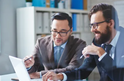 Two professionals seated at a desk collaborating over a laptop and documents, representing trusted administrative support and high-caliber executive assistant talent delivering long-term business impact.