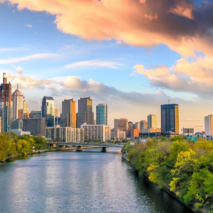 A golden-hour view of Philadelphia’s skyline with modern high-rises, the Schuylkill River, and lush green trees—representing the area served by a leading temp staffing and consulting agency in Philadelphia and Exton.