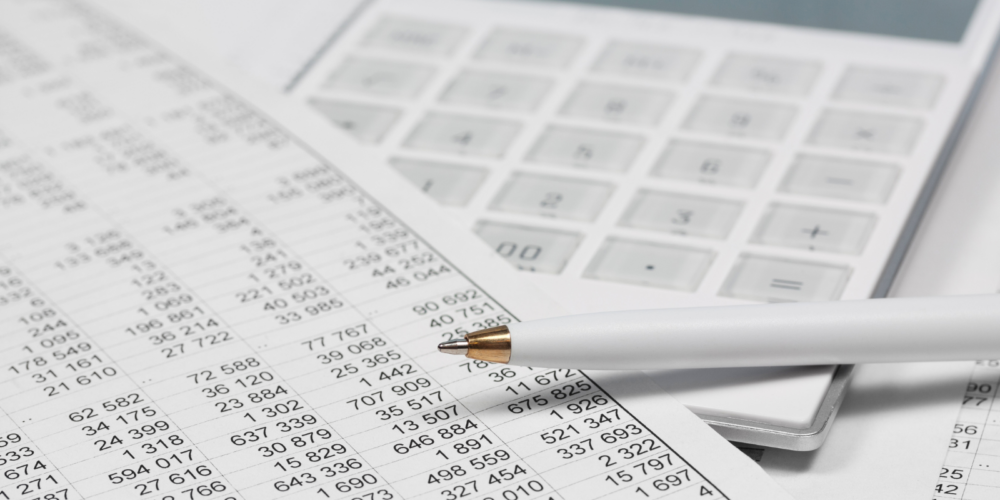 Close-up of a financial spreadsheet with numeric data, a white pen, and a calculator, representing taxation and tax-related calculations.